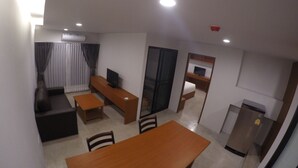 A compact living space with a dining table, a sofa, a TV, and a kitchenette. - Kanith Place (Chiang Mai)
