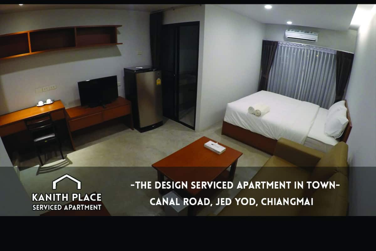 A serviced apartment with a bed, TV, refrigerator, and a desk with a chair.