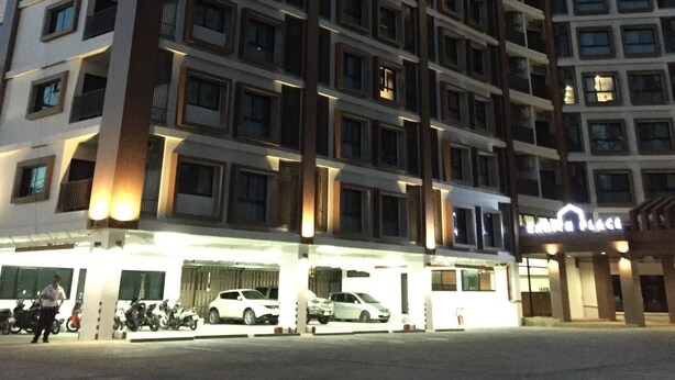 A multi-story hotel named "KANITH PLACE" with illuminated signage, a parking area with several cars, and a security guard standing near the entrance. - Kanith Place (Chiang Mai)