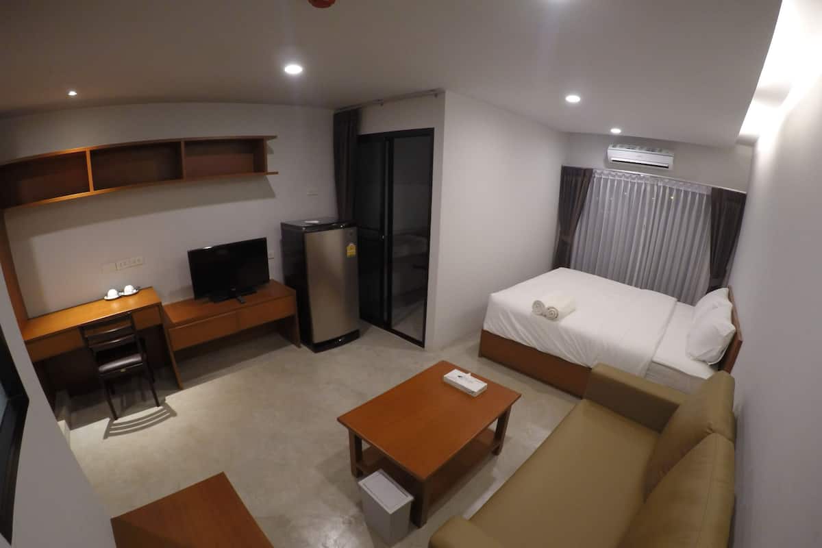 A hotel room with a bed, a desk with a chair, a small refrigerator, a television, and a sofa.
