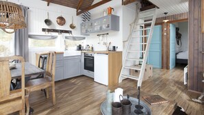 Une cuisine rustique avec un plancher en bois, un coin repas avec une table et des chaises, et une chambre à coucher située en mezzanine, accessible par une échelle.