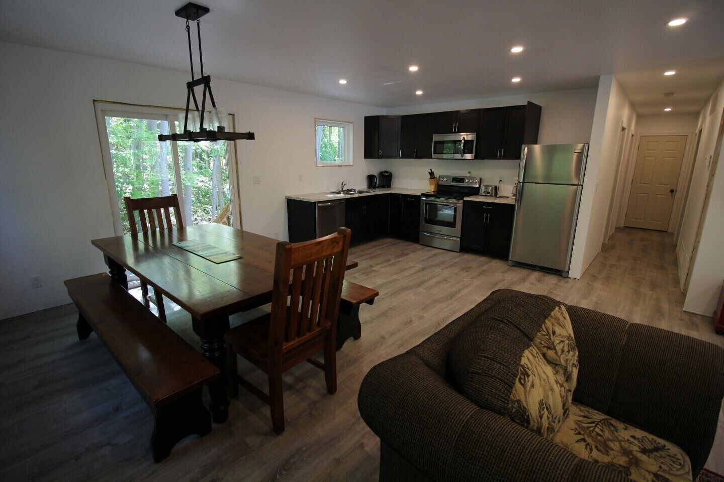 A compact kitchen with dark cabinets, a dining table with benches, a sofa, and a chandelier.