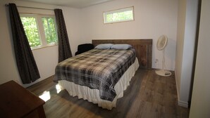 Un dormitorio con una cama, un ventanal, un ventilador de techo y suelo de madera.