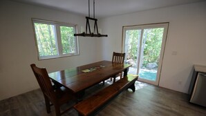 Comedor con una mesa de madera, bancos y sillas. Hay dos ventanas y una puerta que da a un balcón.