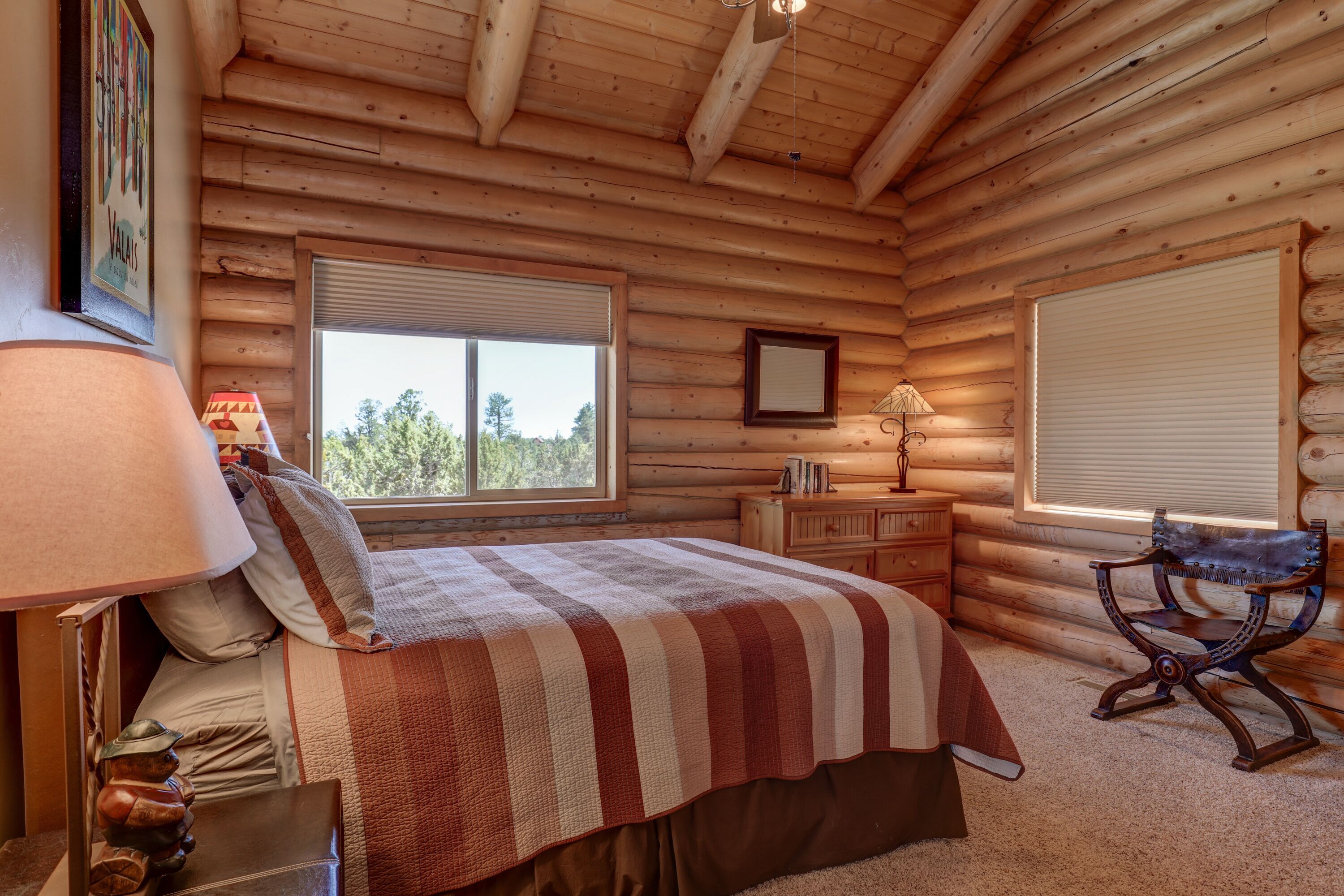 Ein Schlafzimmer in einer Blockhütte mit einem Bett, einem Sessel, einer Kommode und zwei Fenstern.