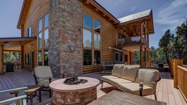 A log cabin with a deck featuring outdoor seating, a fire pit, and a large stone fireplace.