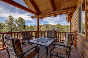 Terraza de madera con cuatro sillas y una mesa, con vistas a un paisaje montañoso.