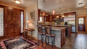 A spacious kitchen with wooden cabinets, a large island with bar stools, a stainless steel refrigerator, and pendant lighting.