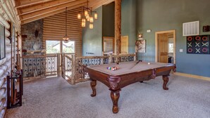 A spacious room with a pool table, wooden ceiling beams, and a stone wall.
