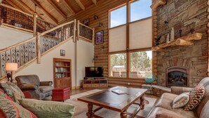A log cabin interior with a wooden staircase, a fireplace, a television, and a cozy seating area.
