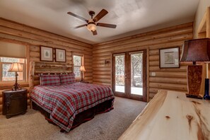 Un dormitorio de cabaña de madera con cama, ventilador de techo y ventanas amplias.