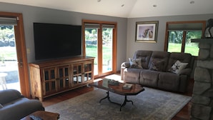 A living room with a large flat-screen TV, a stone fireplace, and a comfortable seating area with a sofa and recliner.