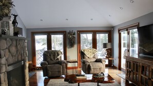 A spacious living room with a stone fireplace, two comfortable armchairs, a coffee table, and a large TV.