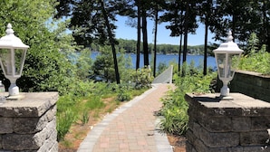 A paved pathway leading to a lake, flanked by stone walls and white lanterns.