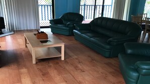 Un soggiorno con un tavolino in legno, due divani in pelle verde e una zona pranzo con sedie in legno.