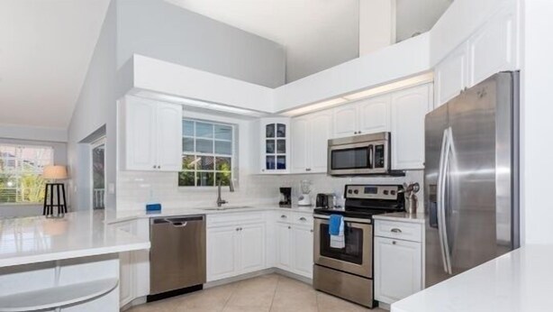 A modern kitchen with white cabinetry, stainless steel appliances, and a large island with a sink.
