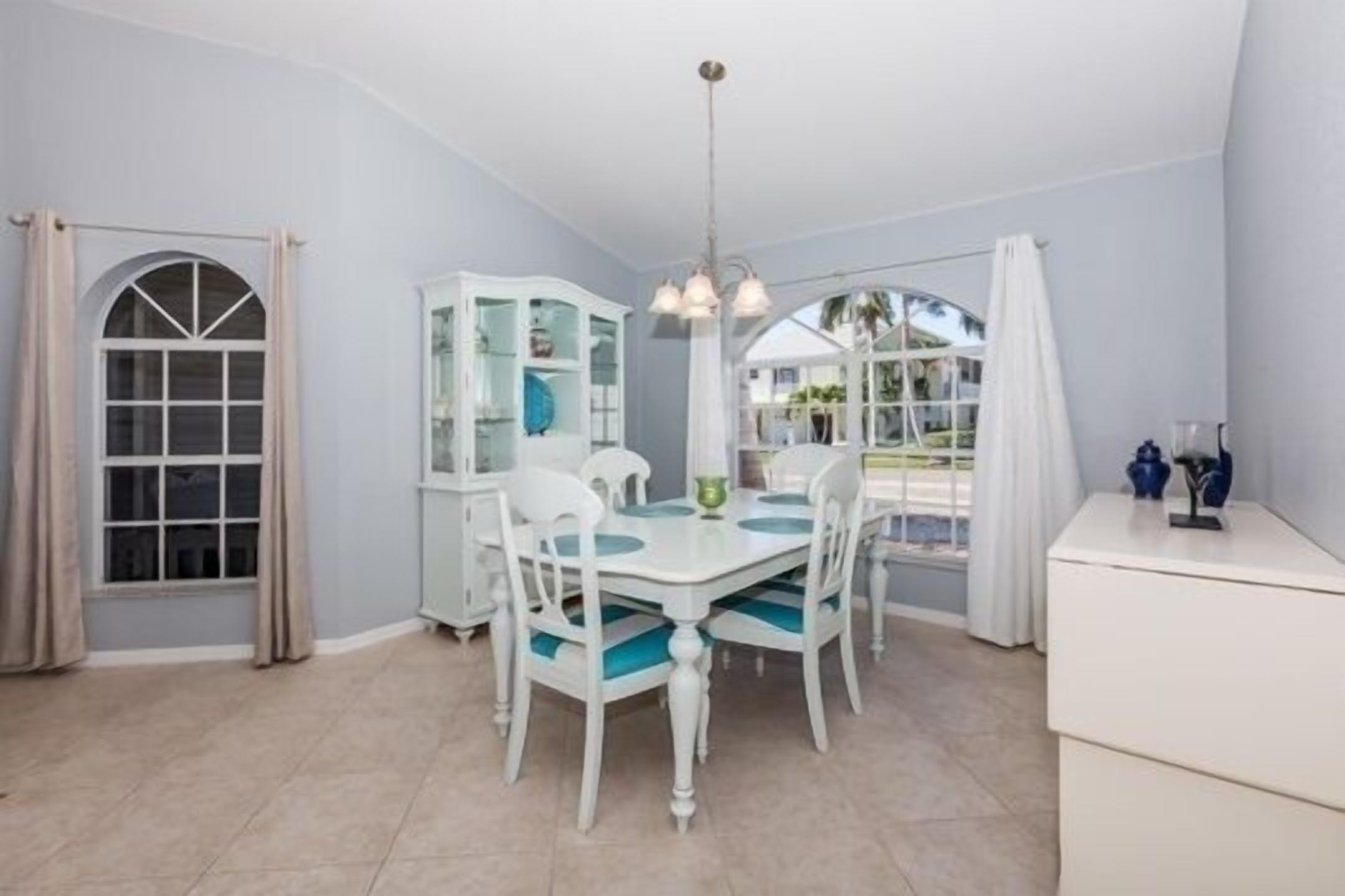 A dining area with a white table and chairs, a glass cabinet, and a view through a large window.
