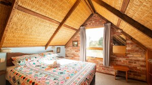 A cozy attic bedroom with a sloped ceiling, a brick wall, and a large window.