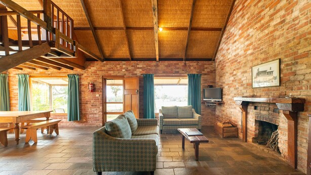 A rustic interior with a wooden staircase, brick walls, a fireplace, and a dining area.