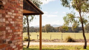 A brick building with a wooden pergola, a grassy field, and trees in the background.