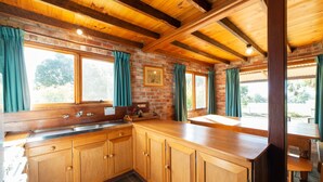 A kitchen with wooden cabinets, a stone backsplash, and large windows with curtains.