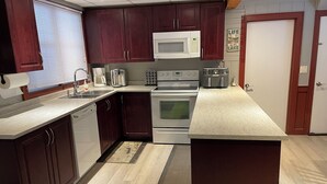 A modern kitchen with dark wood cabinets, a white microwave, a stove, and a coffee maker. - 4 Bedroom Cottage On Manitoulin Island, Ontario (Providence Bay)