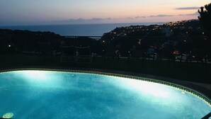 En swimmingpool med utsikt över en kuststad i skymningen.