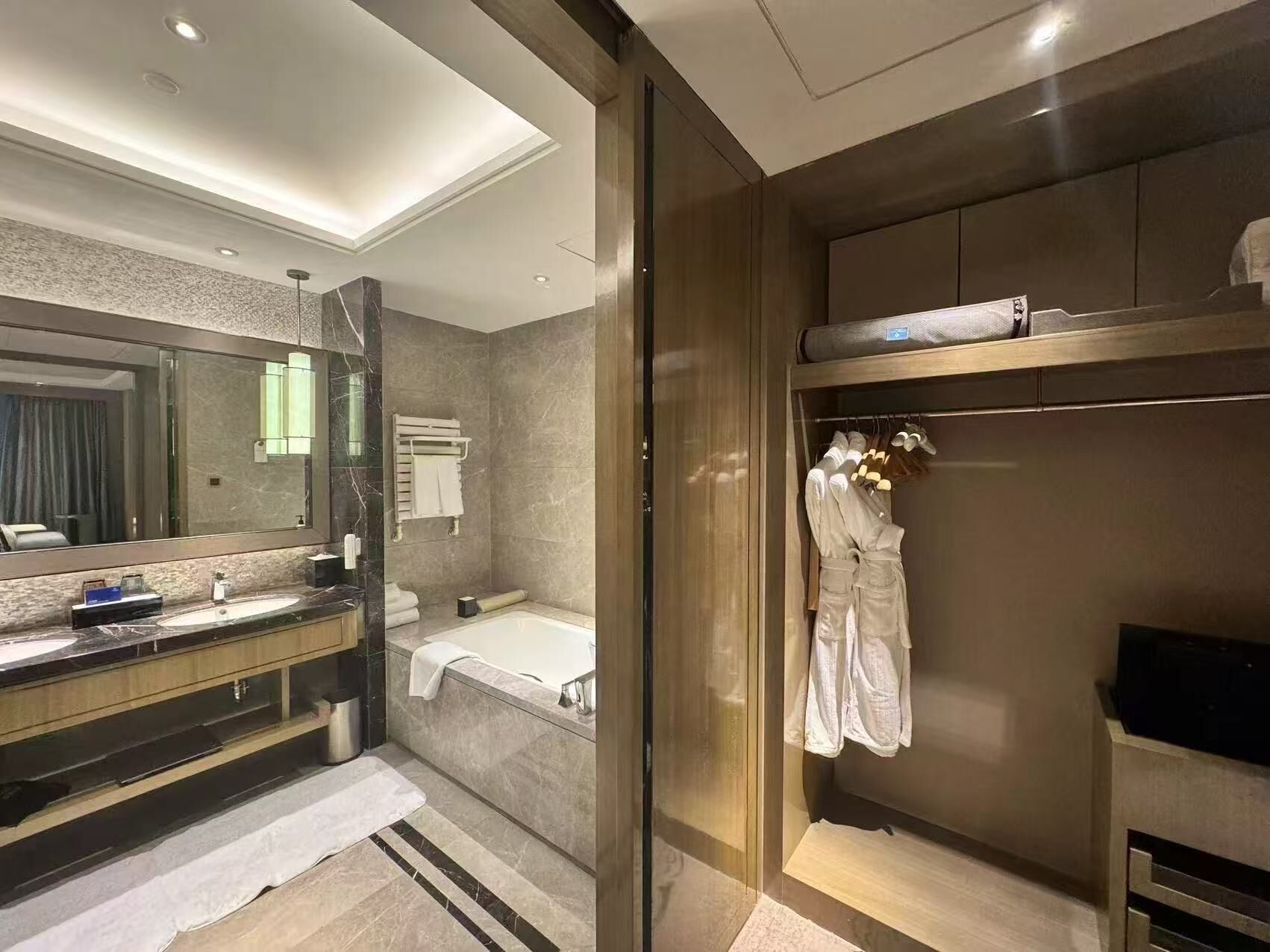 A modern bathroom with a large mirror, a bathtub, a vanity with a sink, and a walk-in closet with hanging robes.