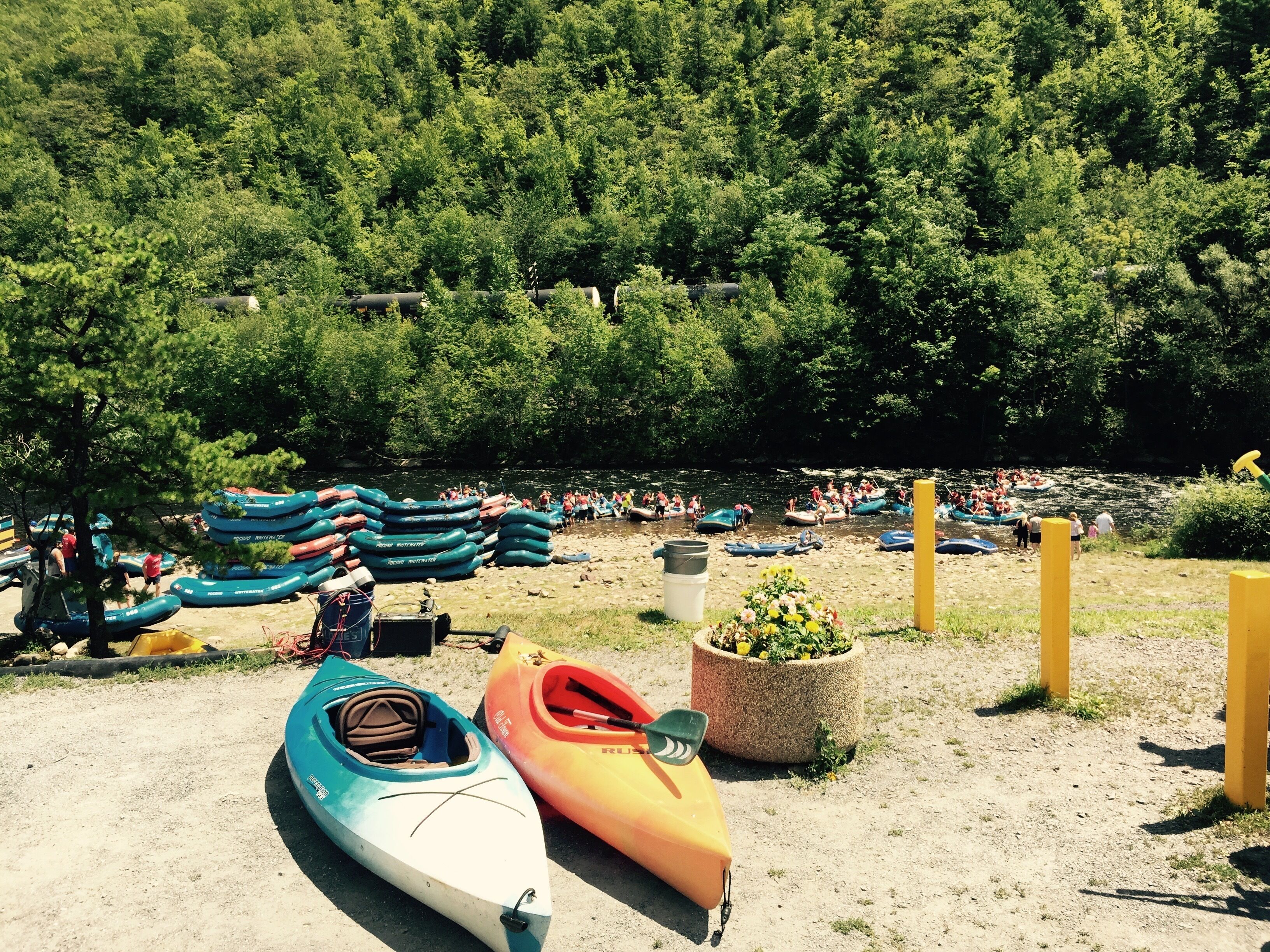 A riverside campsite with canoes and kayaks, surrounded by dense forest.