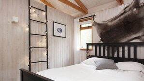 A bedroom with a wooden bed frame, a ladder, a framed picture, and a window with curtains. - Múlakot 5 - Cosy cabin, View the amazing view´s from the porch (Borgarbyggð)