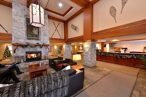 Welcome to our lobby, featuring a cozy fireplace, comfortable seating, and a high ceiling with wooden beams.