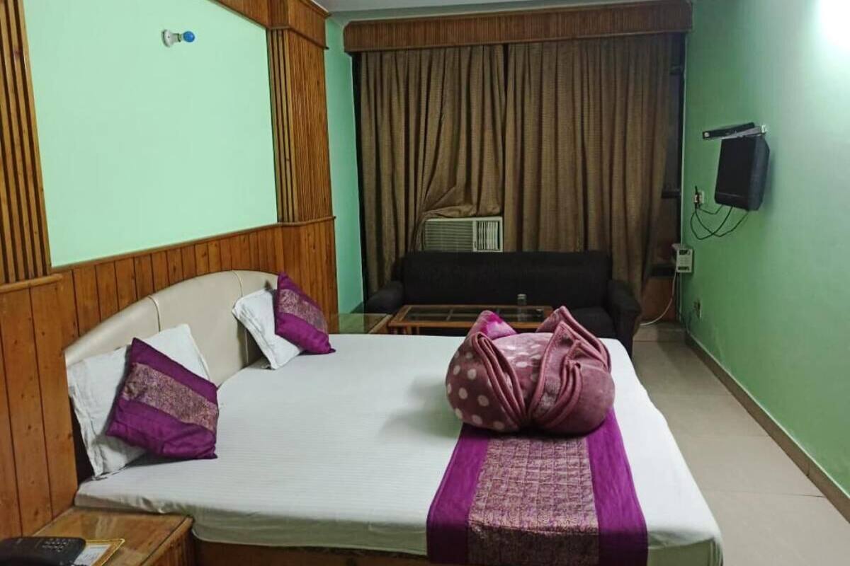 Una habitación de hotel con una cama, cabecero de madera, televisor y cortina.