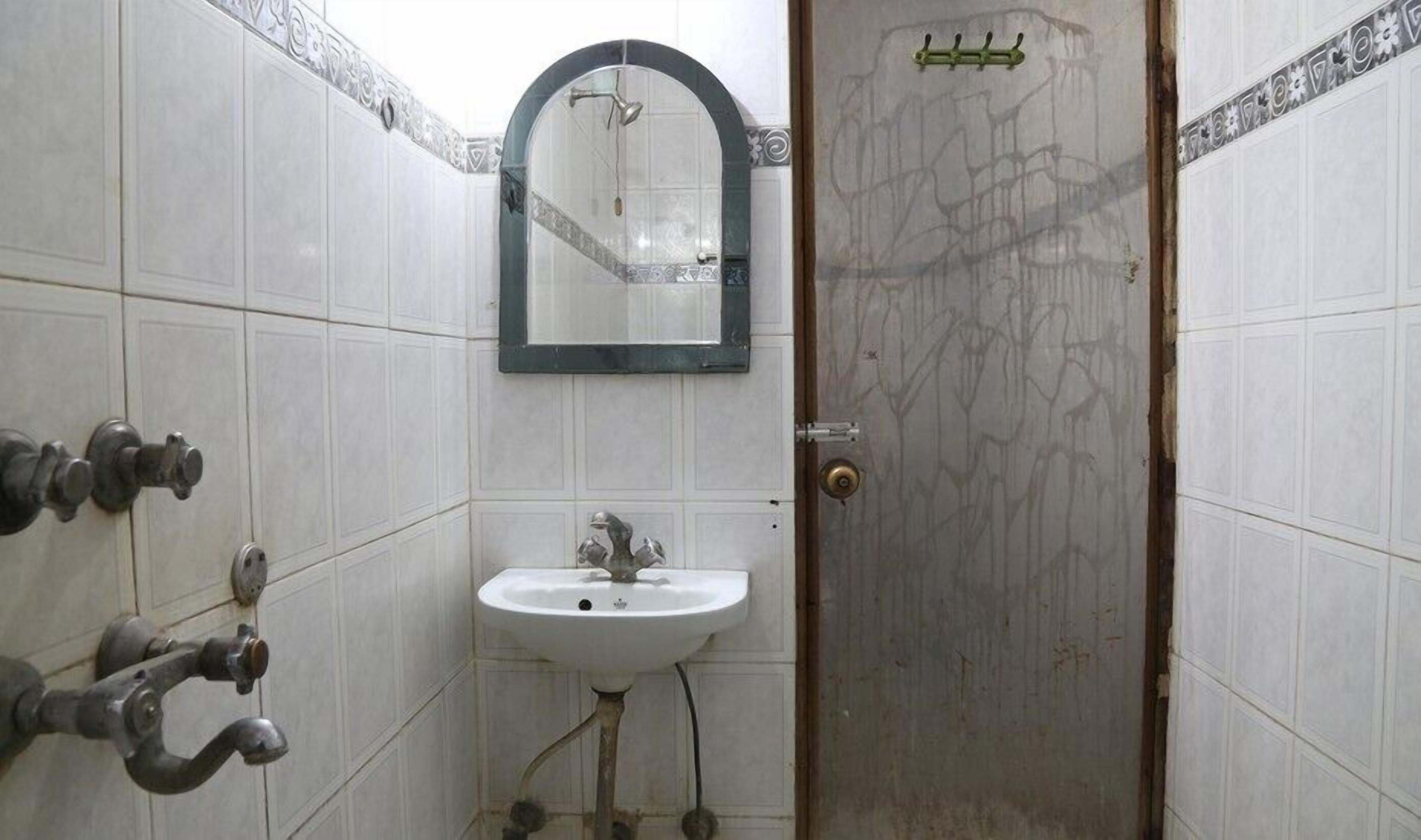 A bathroom with a white sink, a mirror, and a shower. There are pipes and a door with a handle.