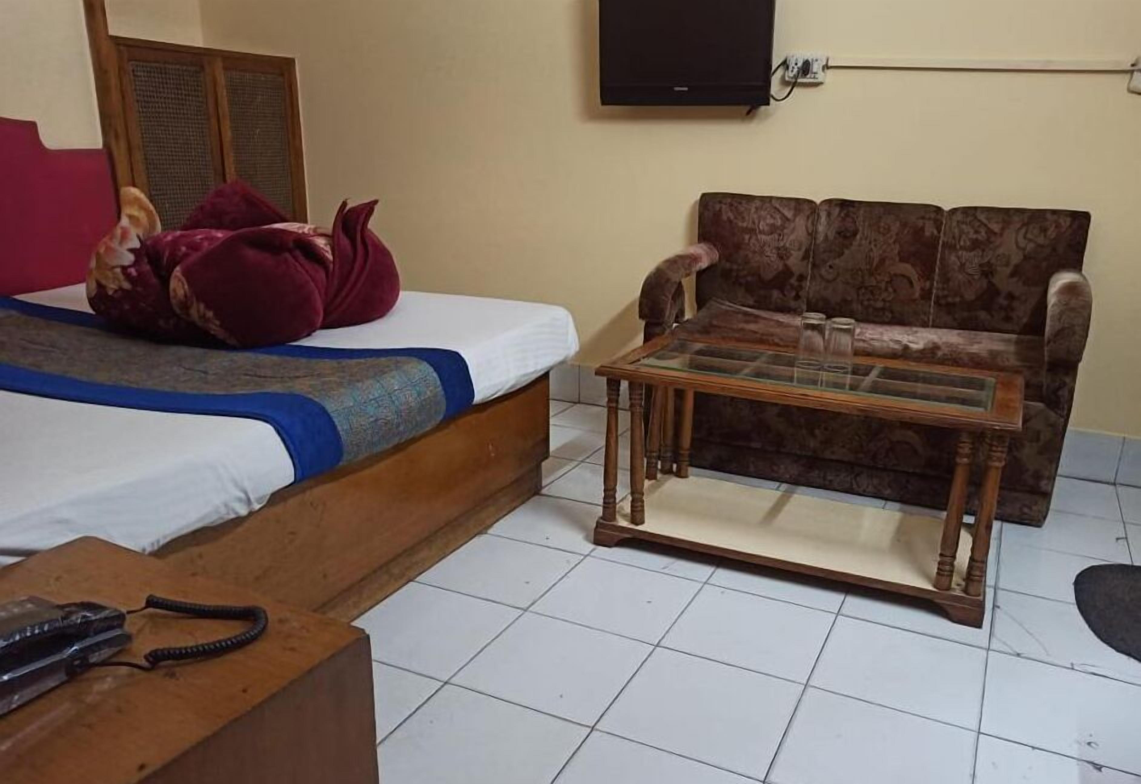 A room with a bed, a sofa, a coffee table, and a television on the wall.
