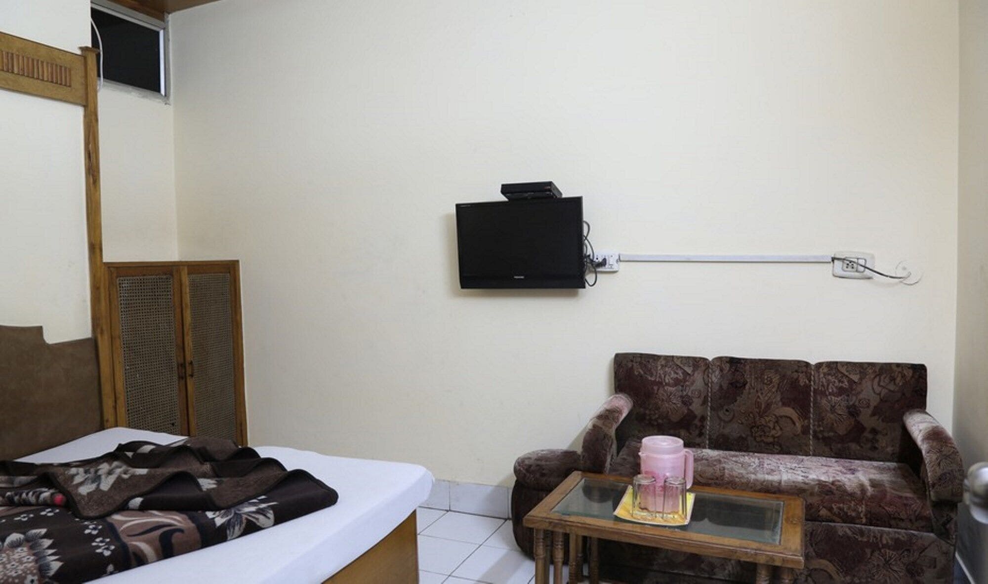 A bedroom with a bed, a sofa, a small table with a pink mug, and a TV mounted on the wall.