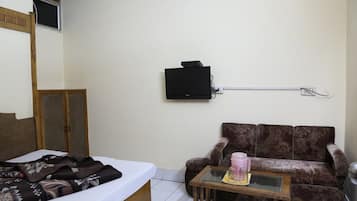 A bedroom with a bed, a sofa, a small table with a pink mug, and a TV mounted on the wall.