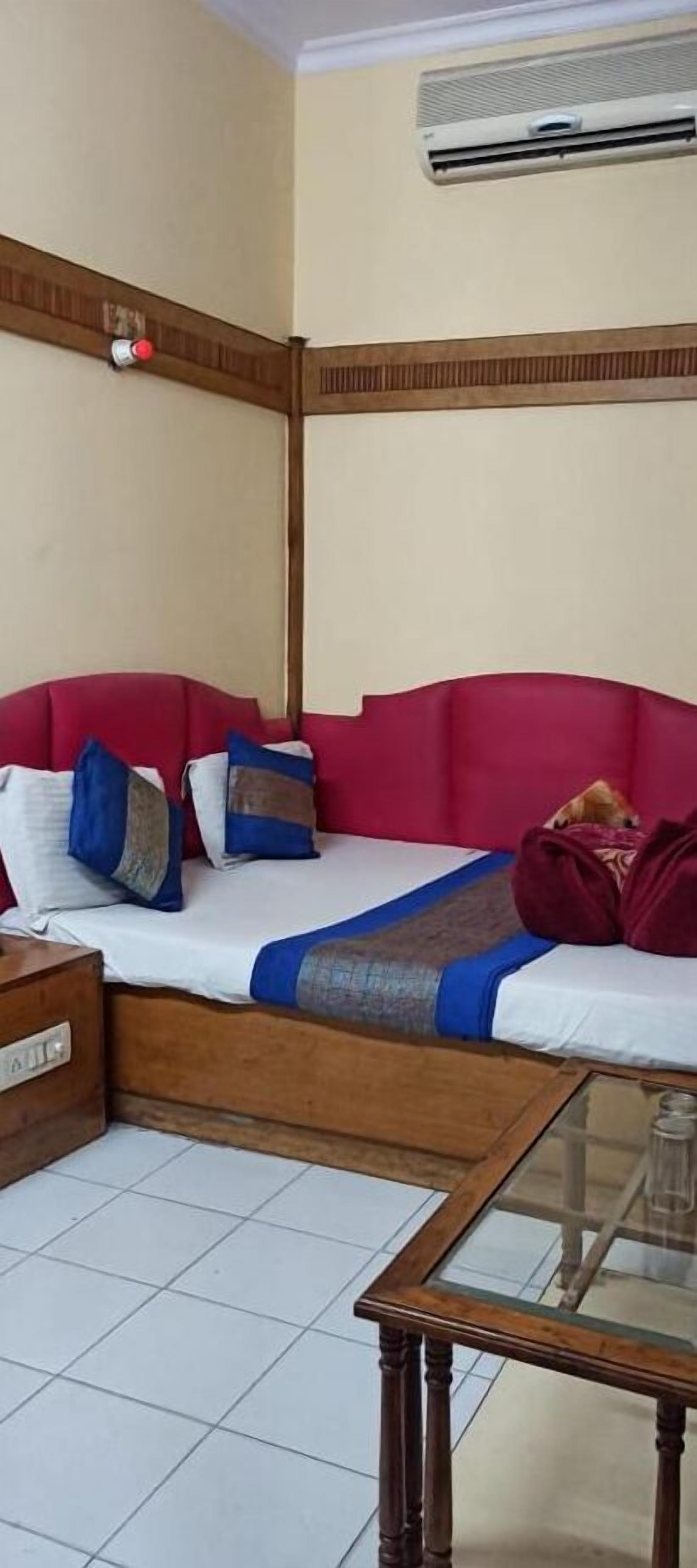 Une chambre avec un lit, une table de chevet en bois, une table avec un plateau en verre et un appareil de climatisation fixé au mur.