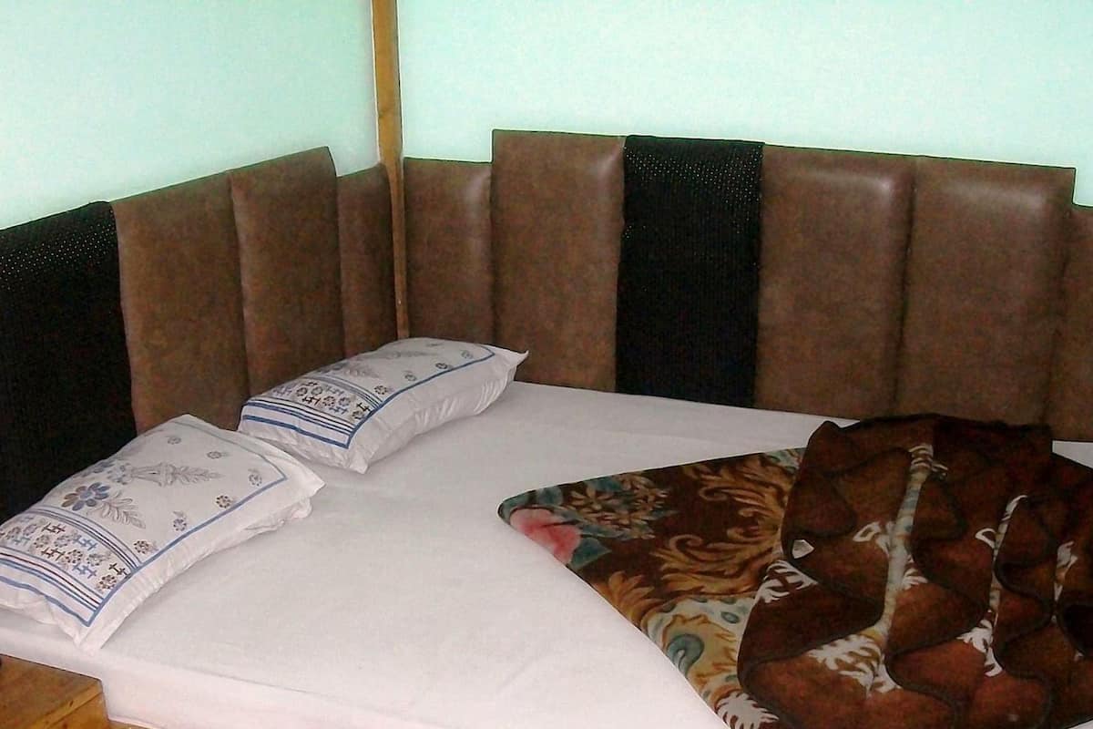 Una cama de madera con colchón blanco, dos almohadas y una manta marrón.