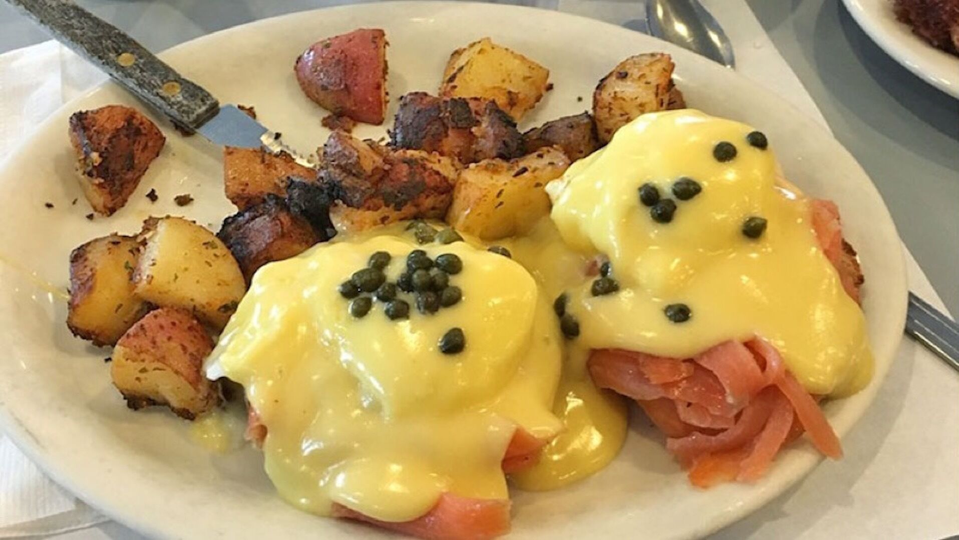 A plate of eggs benedict with ham and potatoes.