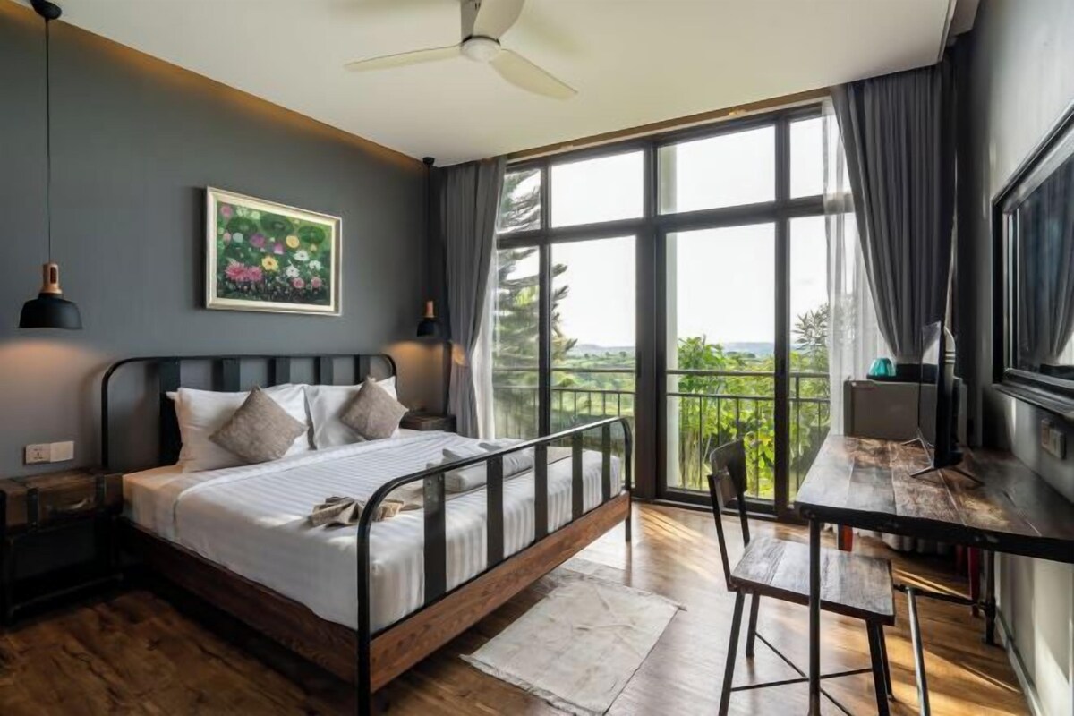 A bedroom with a bed, a desk, and a balcony with a view.