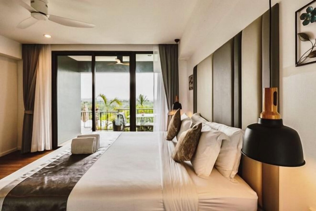 A hotel room with a large bed, a ceiling fan, a view of the outdoors, and a modern lamp.