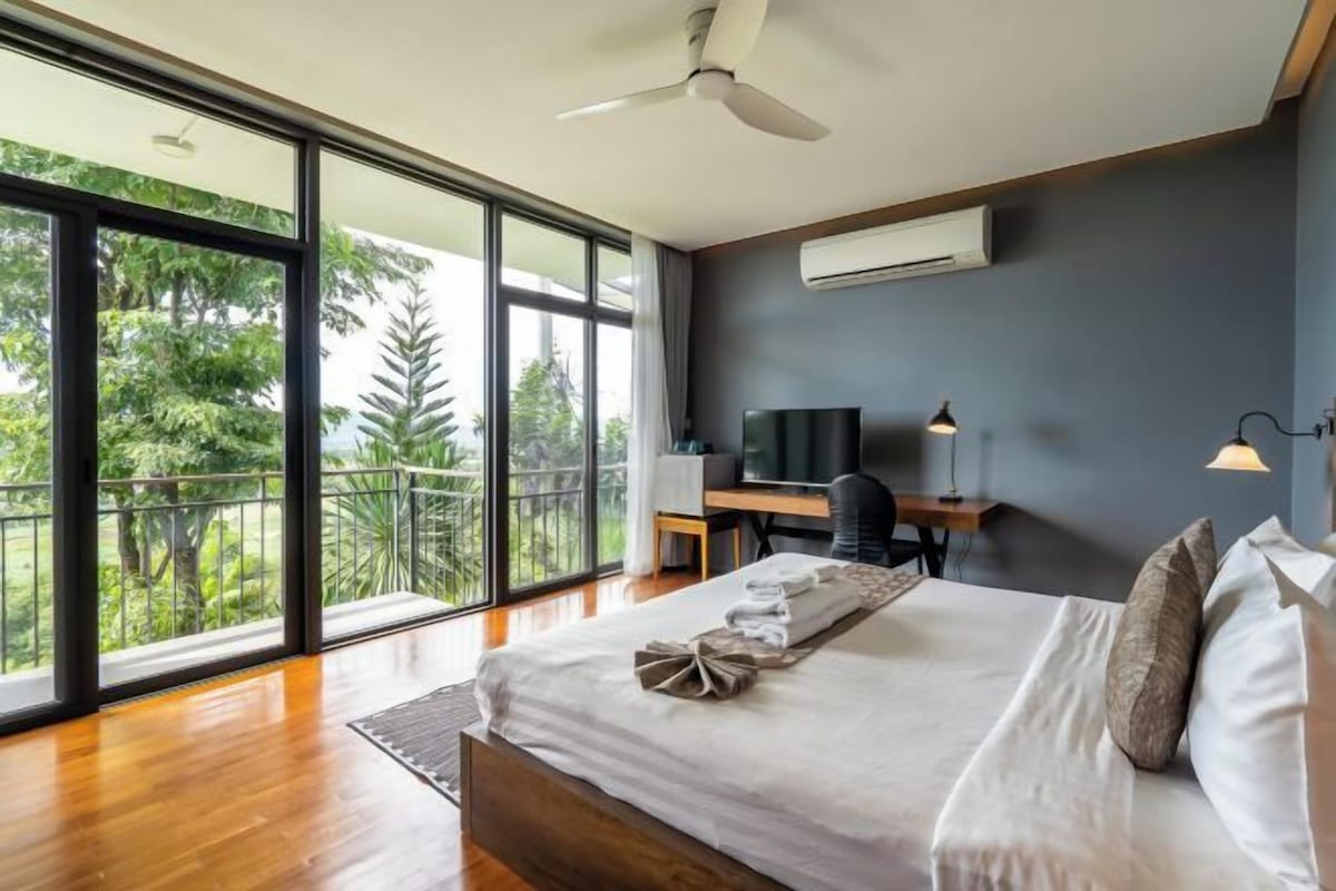 Een moderne hotelkamer met een groot bed, een bureau, een televisietoestel en een balkon met uitzicht op groen.