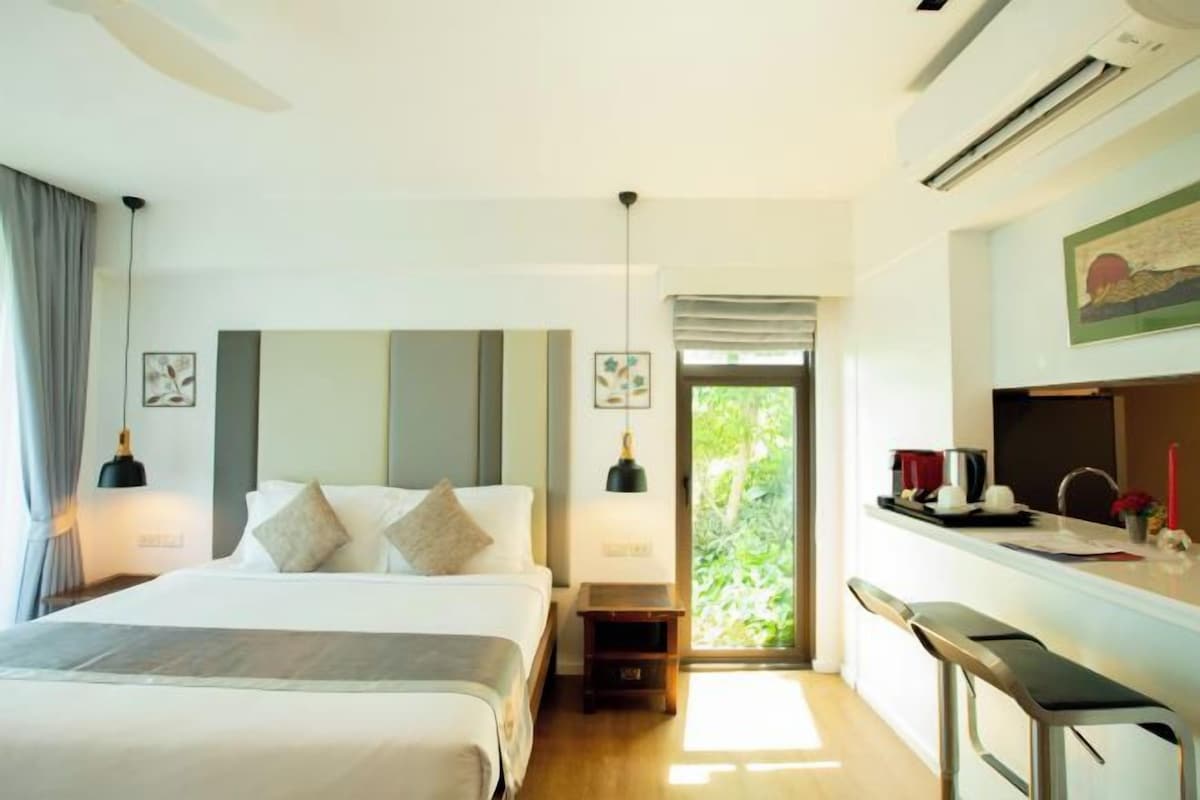 Een moderne hotelkamer met een groot bed, een bureau met een stoel en uitzicht op groen door het raam.