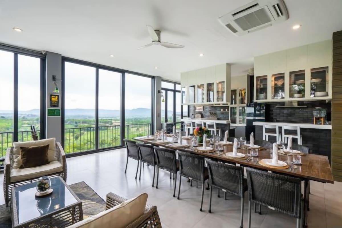 Een ruime eetruimte met een lange tafel gedekt voor zes personen, omringd door stoelen. Een balkon met uitzicht op het landschap is zichtbaar door grote ramen.