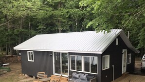 Eine kleine Holzhütte mit einer Terrasse, Sitzgelegenheiten im Freien und einem großen Schiebeglastür.