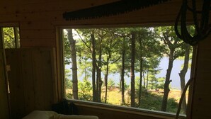 Ein Zimmer mit großem Fenster und Blick auf einen Wald und ein Gewässer.