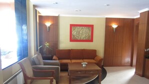 A living room with a sofa, armchair, and coffee table. There are two wall-mounted lights and a framed artwork on the wall. - Hotel Jumolhari (Thimphu)