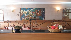 A hotel lobby with a wooden reception desk, a large colorful painting on the wall, and a basket of fruits on the counter. - Hotel Jumolhari (Thimphu)