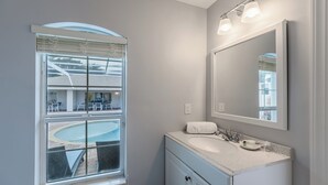 Un baño con una ventana grande, un lavabo, un espejo y vistas a una piscina y zona de estar exterior.
