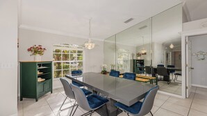 Un comedor moderno con un separador de vidrio, un armario verde y una araña.